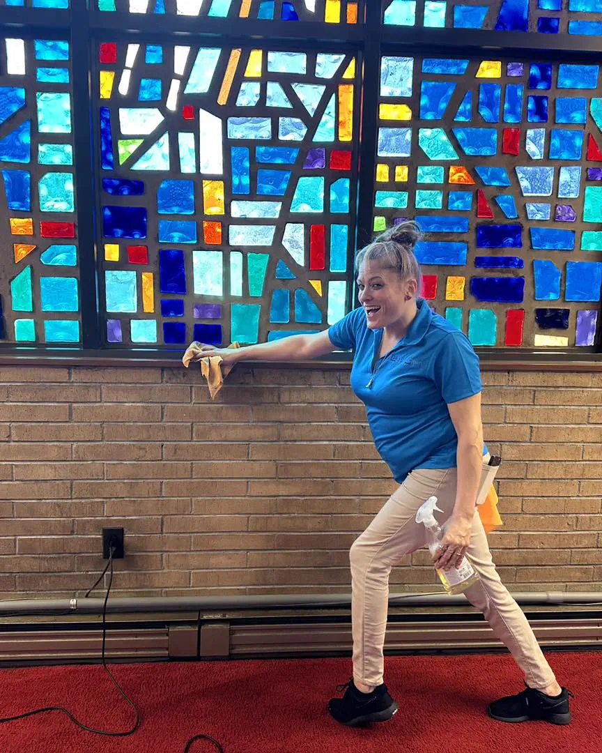 A NuFresh Clean cleaner wiping a sill under a stained-glass window, spray bottle in hand